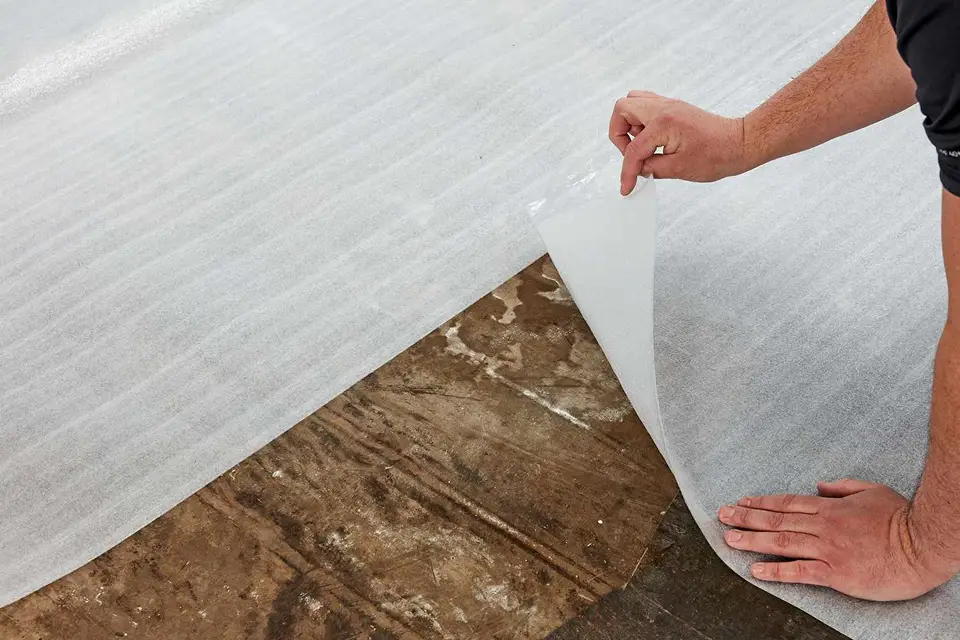 A worker carefully lays down protective sheeting over a subfloor, a crucial preparatory step before new flooring installation in any home renovation.